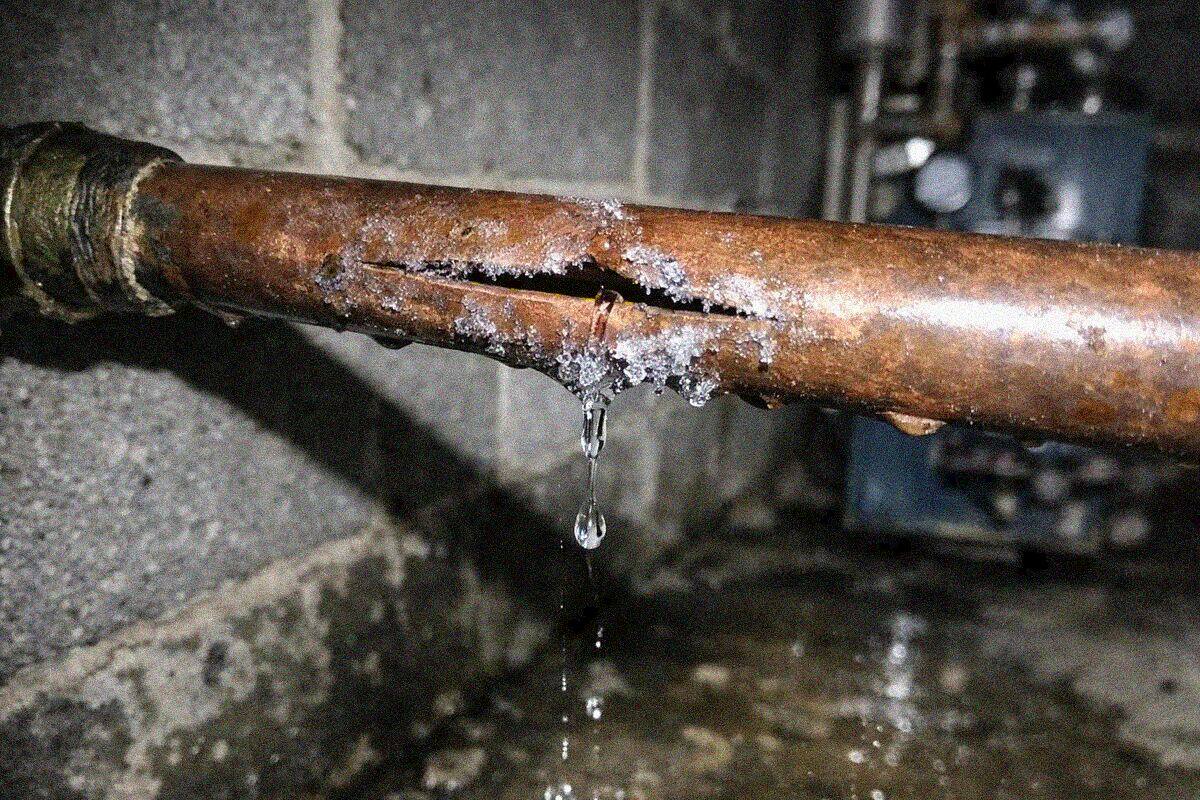 A split section of old galvanized supply pipe in a Queens basement with water pooled on the concrete floor beneath it