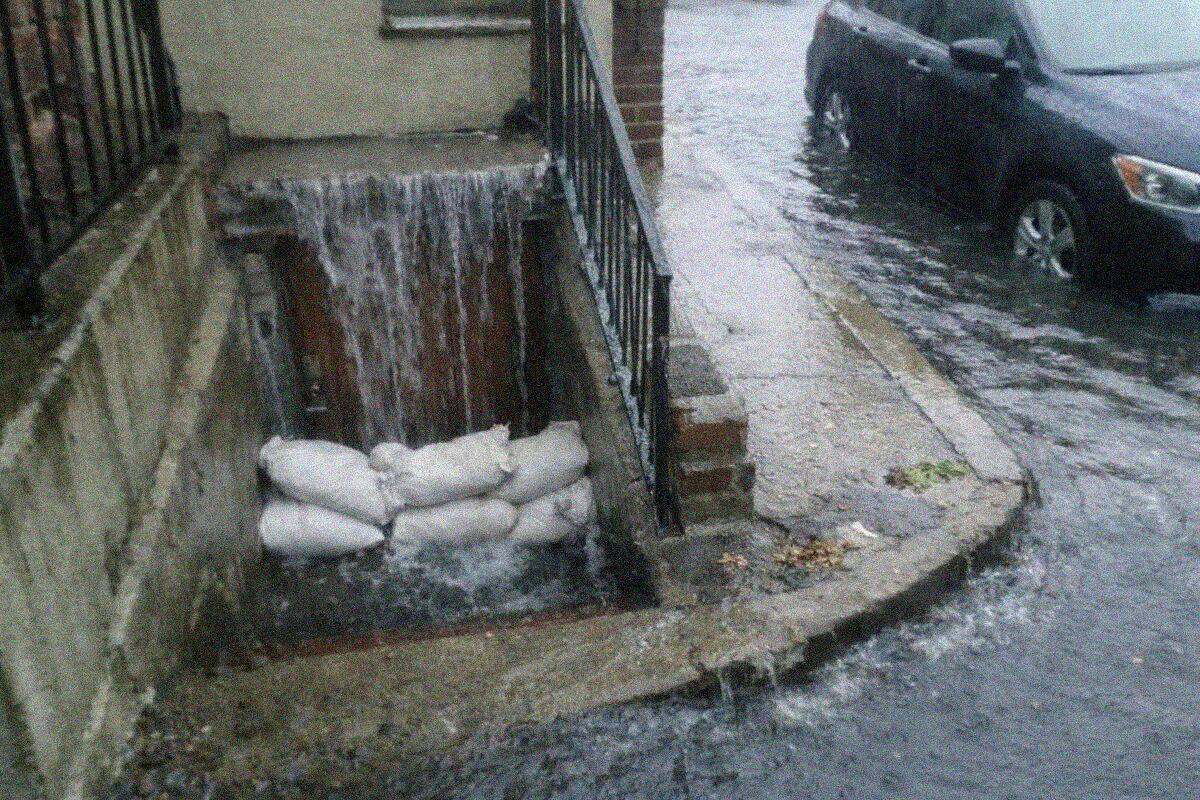 Storm water pouring down an exterior stair into the doorway of a basement apartment in Queens